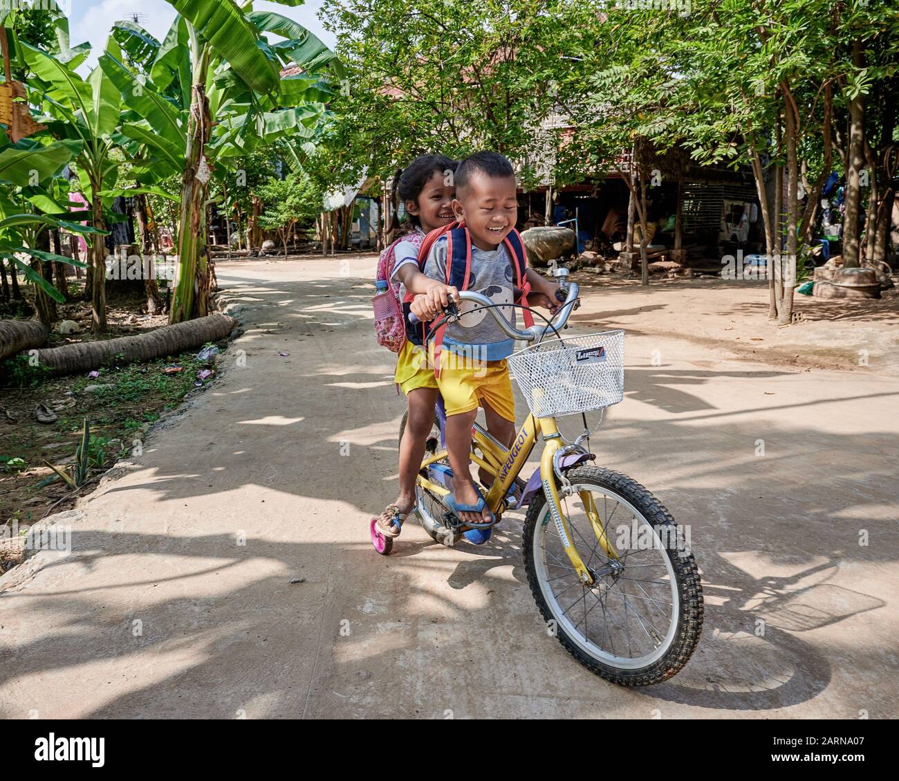 Frère du village rural et soeur à cheval joyeusement sur leur vélo. Enfants d'Angkor Ban prêts pour l'école. Coloré Banque D'Images