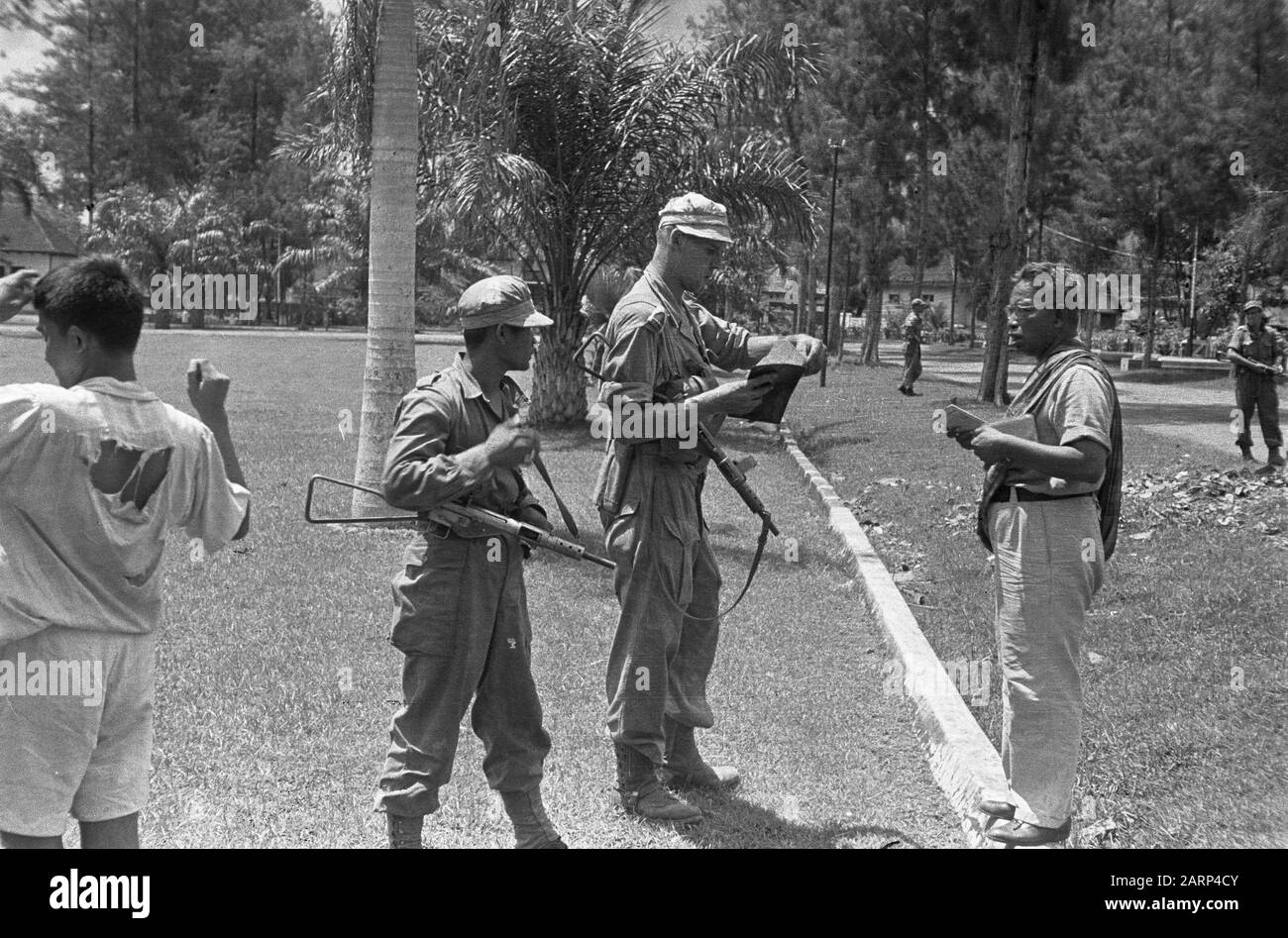Avance de la V-Brigade un soldat néerlandais avec un stengun vérifie les papiers qui lui sont remis par un homme indonésien avec slendang, debout sur une pelouse ( aloon-aloon?) - Oui. Il y a un KNil Miltarian, également armé de stengun. A gauche un garçon avec des vêtements de dessus déchirés Date: 1948/12/01 lieu: Indonésie, Pays-Bas East Indies Banque D'Images