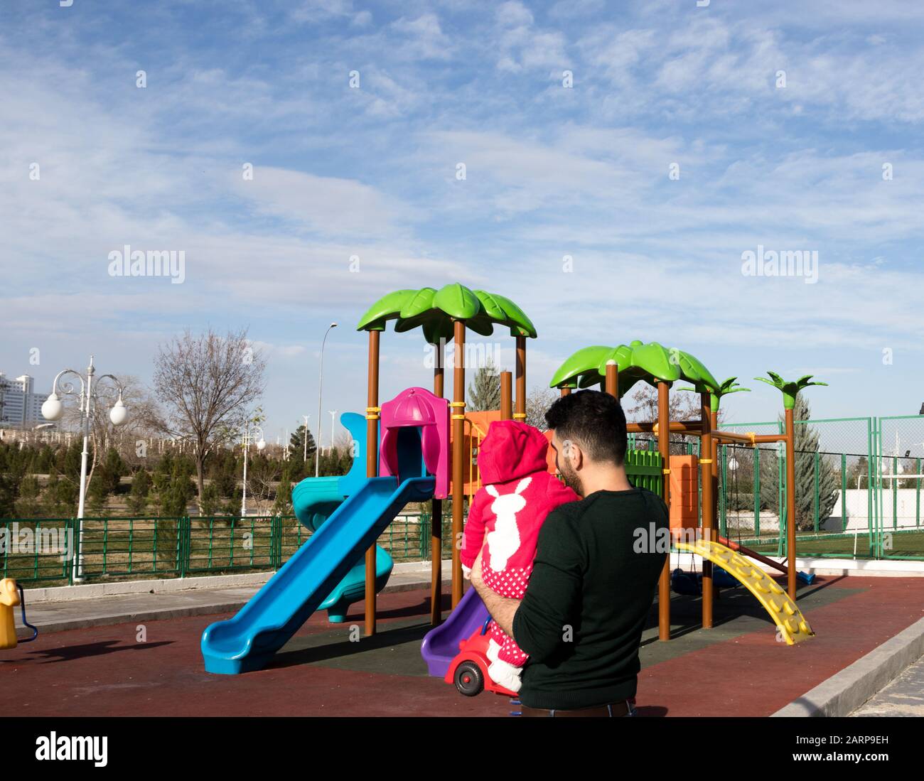 Père et sa fille dehors à l'aire de jeux, une journée ensoleillée avec du ciel bleu à l'arrière-plan. Banque D'Images
