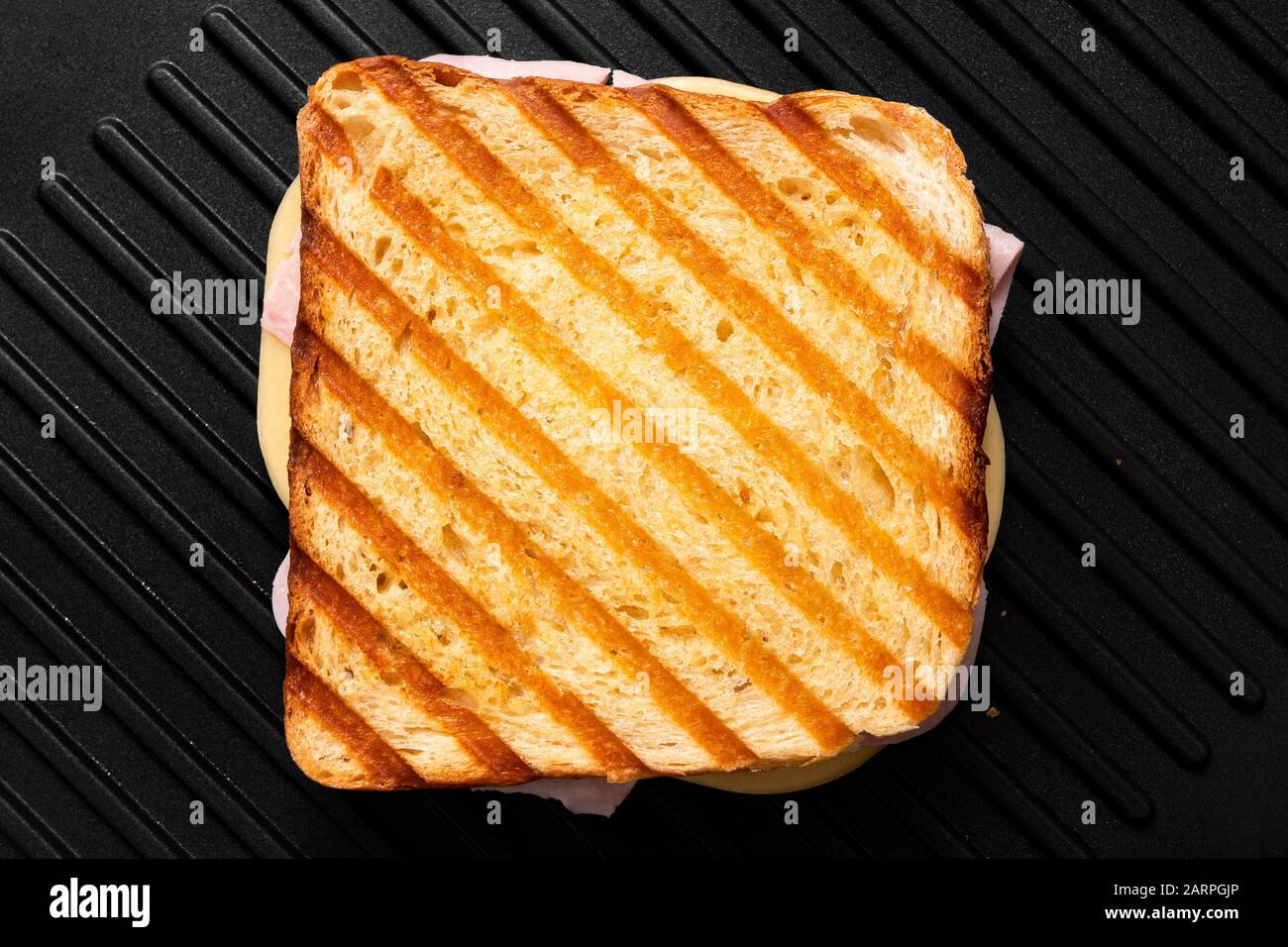 Sandwich au fromage grillé et au jambon avec des marques de gril isolées sur le gril antiadhésif noir. Vue de dessus. Banque D'Images