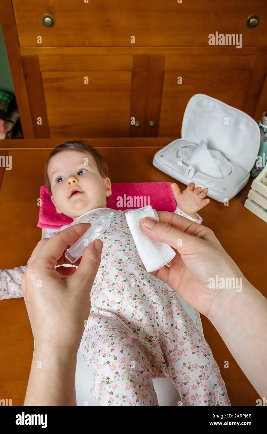 Mains de mère versant sérum pour nettoyer les yeux de bébé Banque D'Images
