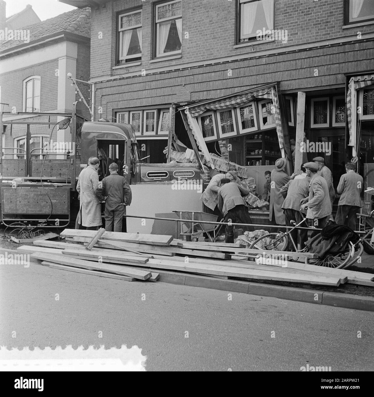 Sturcked, parce qu'il a soudainement vu une voiture de passager venant de la droite, le conducteur d'un camion dans la Dorpsstraat à Heerde a jeté la roue à gauche, a frappé un trottoir et a perdu la puissance sur la roue. Le camion de 17 tonnes a été chargé dans un magasin de matériel et de produits ménagers. Personne du magasin n'a été blessé. Le chauffeur de 32 ans est sorti avec la droite. Son cochauffeur a cassé les deux jambes Date: 5 avril 1957 lieu: Gueldre, Heerde mots clés: Accidents, circulation, camions, magasins Banque D'Images