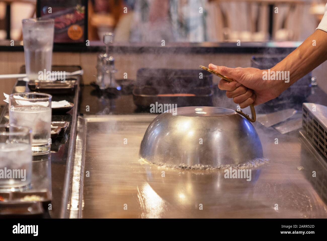 Cuisson sur une poêle japonaise, la surface de cuisson de Tepanyaki. La  cuisinière a couvert les aliments de cuisson avec un couvercle et fait  cuire les aliments à la vapeur. Gros plan