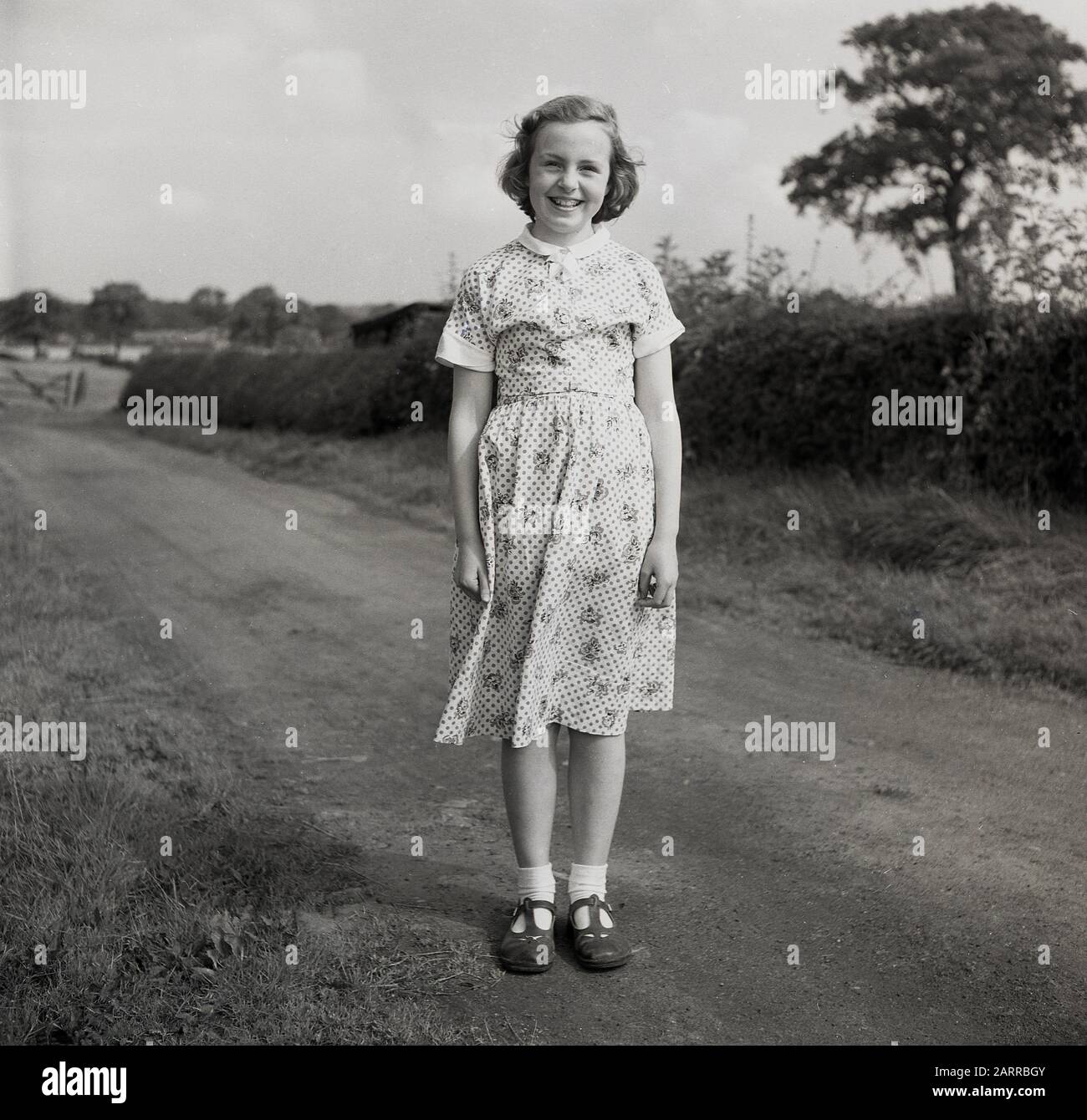 Années 50, historique, fille anglaise dans une robe et portant des sandales debout sur un chemin de pays, Angleterre, Royaume-Uni. Banque D'Images