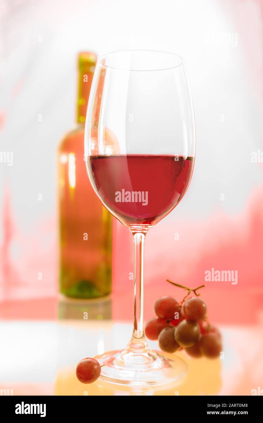 Un verre de vin rouge à l'avant et un peu de raisin, une bouteille floue à l'arrière-plan. Banque D'Images