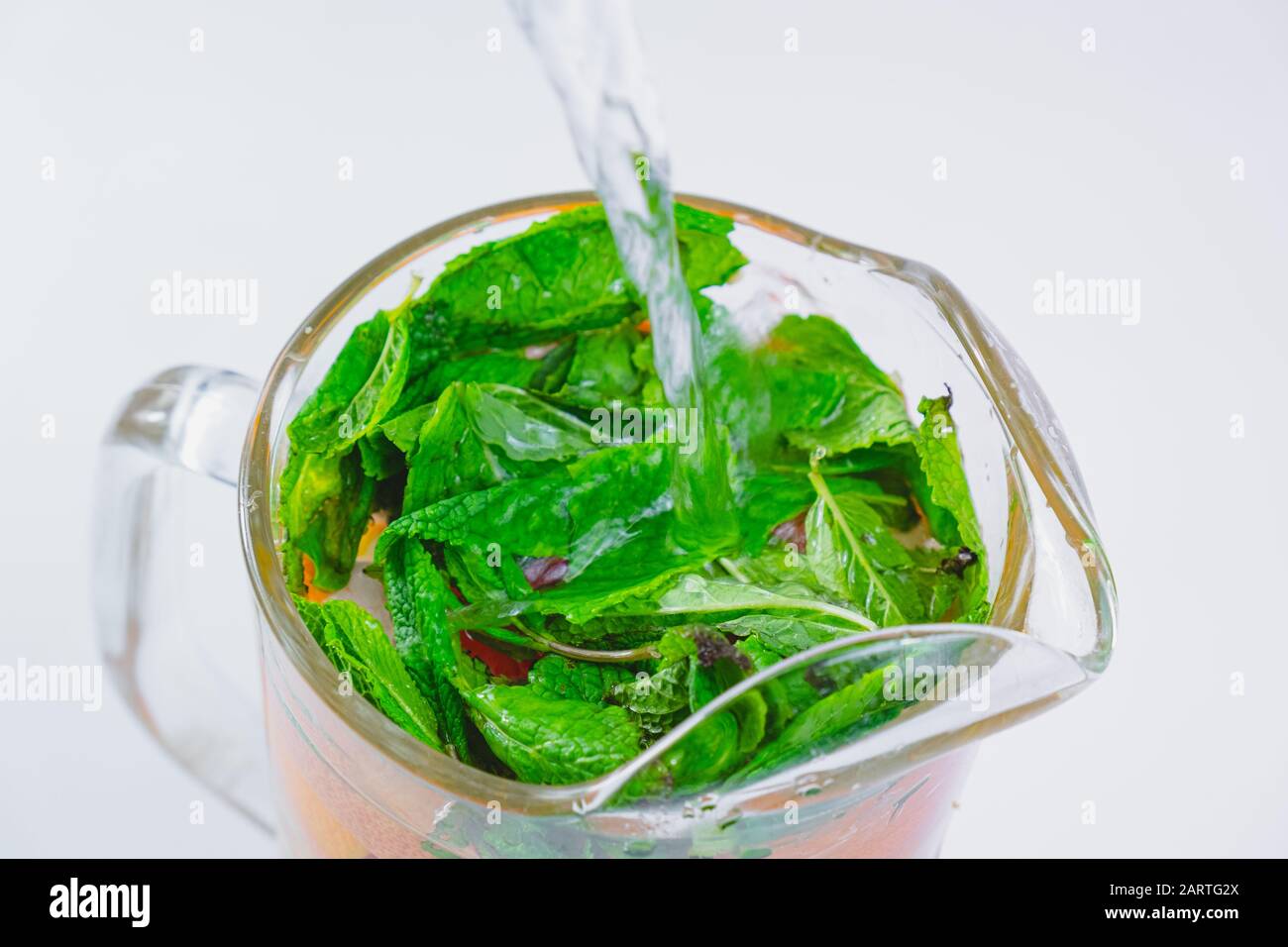Verser de l'eau sur des feuilles de menthe poivrée fraîche et des tranches de pamplemousse dans une vue rapprochée en verre. Préparer de l'eau tonique ou de la limonade, saine boisson fraîche con Banque D'Images