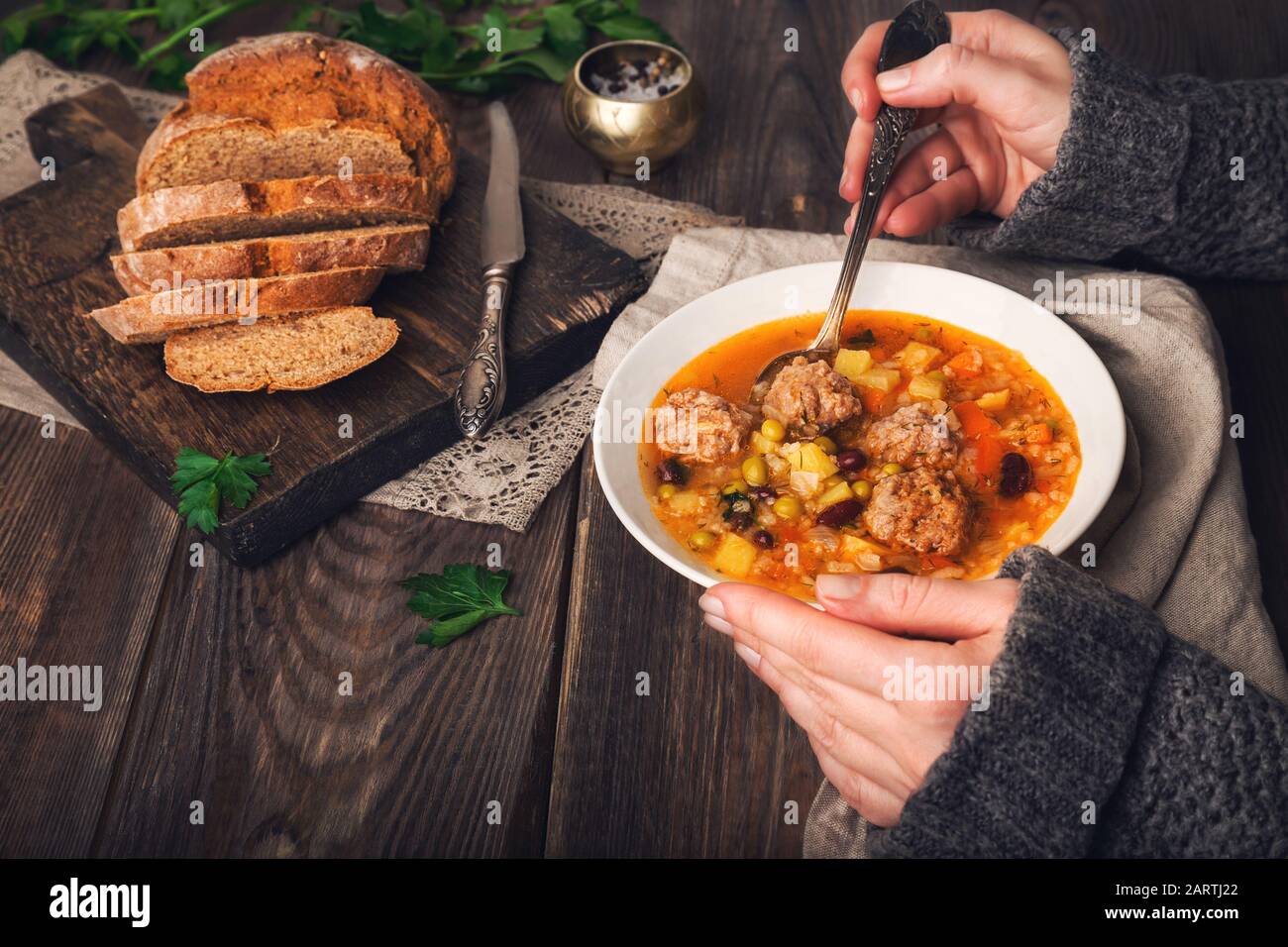 Vue réduite d'une femme mangeant une soupe de légumes avec des boulettes de viande à une table en bois rustique. Banque D'Images