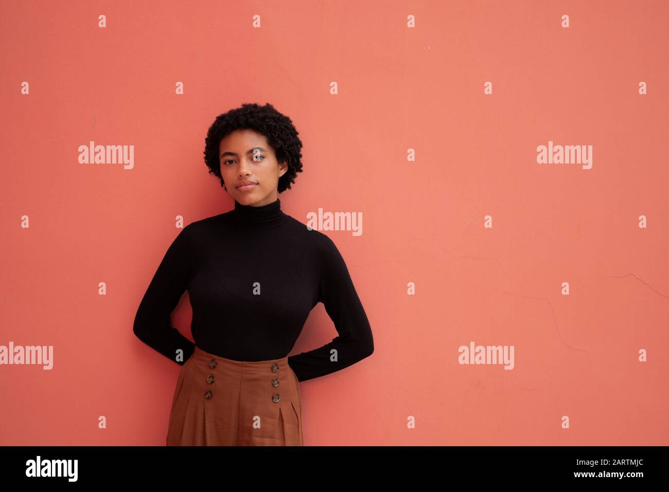 Jeune femme avec des cheveux bouclés debout contre le mur Banque D'Images