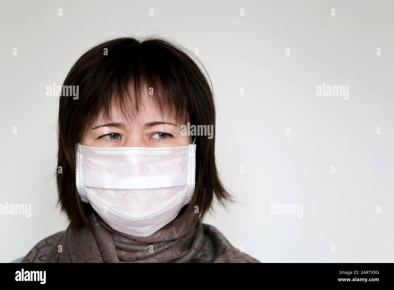Femme dans un masque médical et un foulard enveloppé autour de la gorge sur fond blanc. Concept de maladie, fièvre, symptômes du coronavirus, rhume et grippe Banque D'Images
