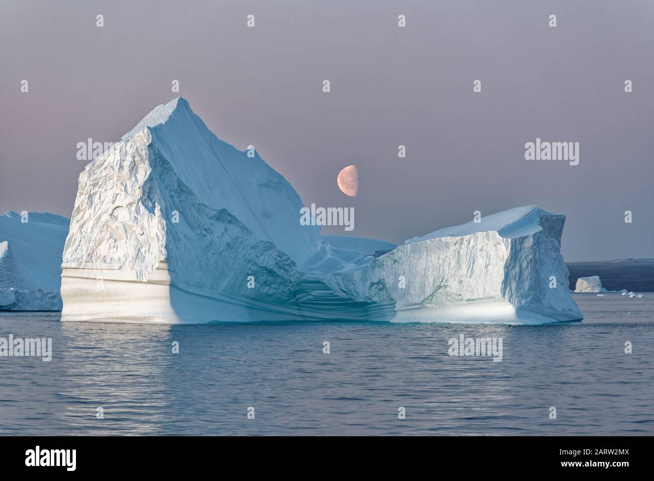 Énorme iceberg flottant dans un fjord au coucher du soleil avec lune au milieu, fjord, Scoresby Sund, Kangertittitaq, Groenland,Danemark Banque D'Images