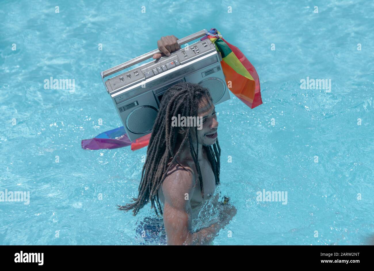 Bel homme noir tenant une cassette radio à l'ancienne avec le drapeau de  fierté gay dans la piscine. Gay et concept amusant Photo Stock - Alamy