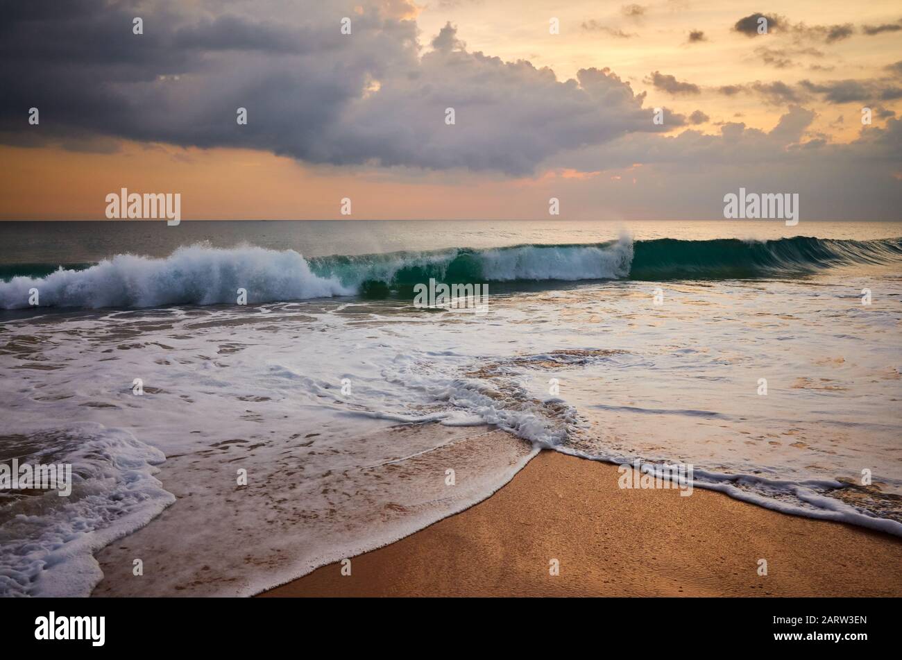 Plage tropicale avec une vague d'écrasement au coucher du soleil doré. Banque D'Images