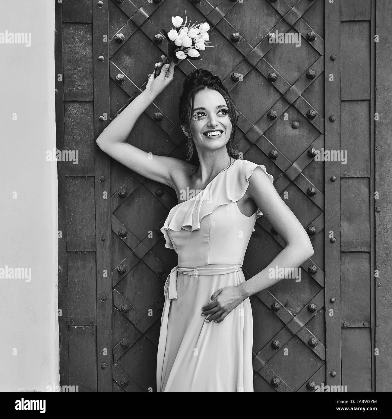 Belle demoiselle de demoiselle de demoiselle fille brunette porte élégante pleine longueur tulipe une robe de femme de chambre d'épaule et tenant bouquet de fleurs. Vieille ville européenne Banque D'Images