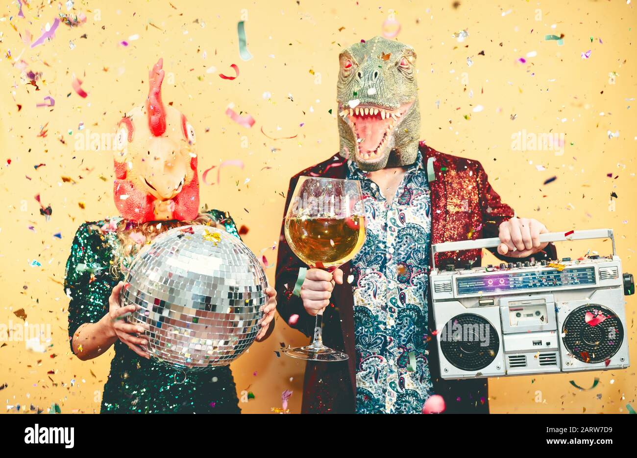 Couple fou célébrant la veille du nouvel an portant un masque de poulet et de dinosaure t-rex - jeunes gens branchés qui ont du champagne et de la musique à l'écoute Banque D'Images