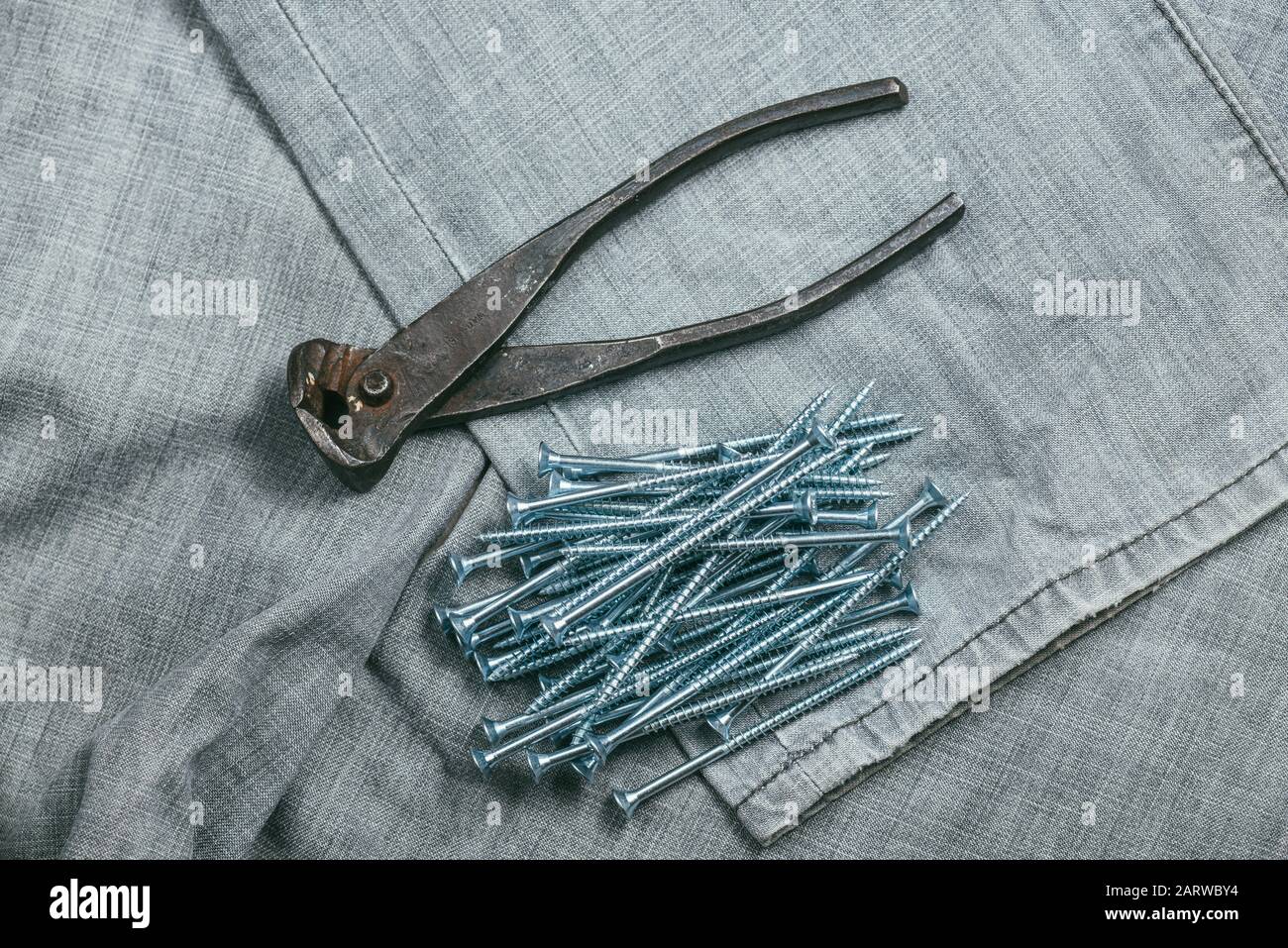 Une poignée de vis autocoupantes métalliques et de pinces très vieilles et rouillées se trouve sur fond d'un vieux tissu denim. Prise de vue macro avec mise au point sélective avec Banque D'Images