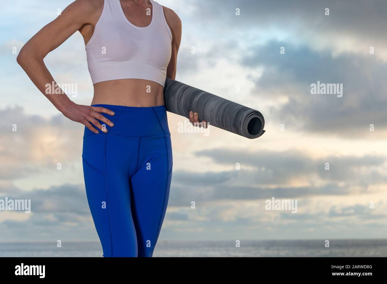 femme avec tapis de yoga est prêt pour la forme physique. Femme ajustée,  saine et sportive dans des vêtements de sport. Femme tenant roulé tapis  d'exercice à l'extérieur près de l'océan Photo