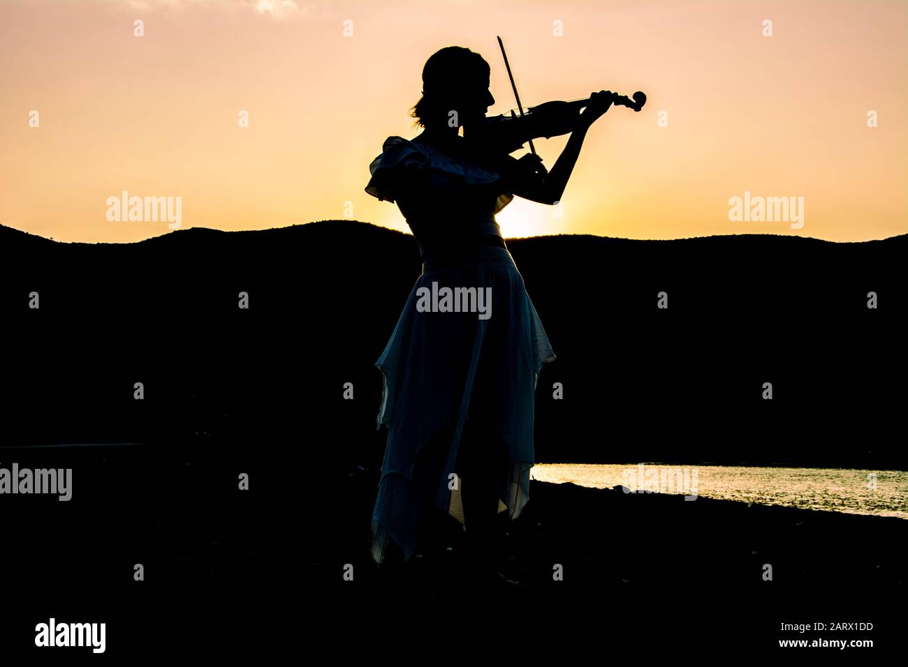 Silhouette d'une femme jouant au violon sur la plage Banque D'Images