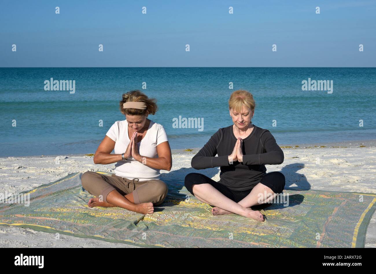 Deux Belles femmes d'âge mûr faisant du yoga au lever du soleil sur la plage Banque D'Images