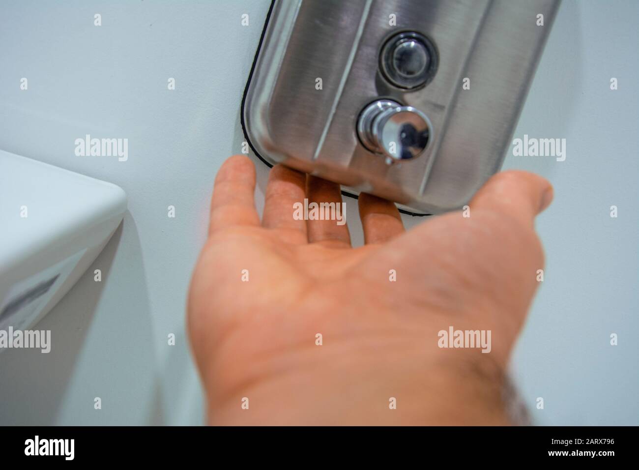 Gros plan de la main masculine essayant d'obtenir du savon du distributeur de savon liquide sur le mur Banque D'Images