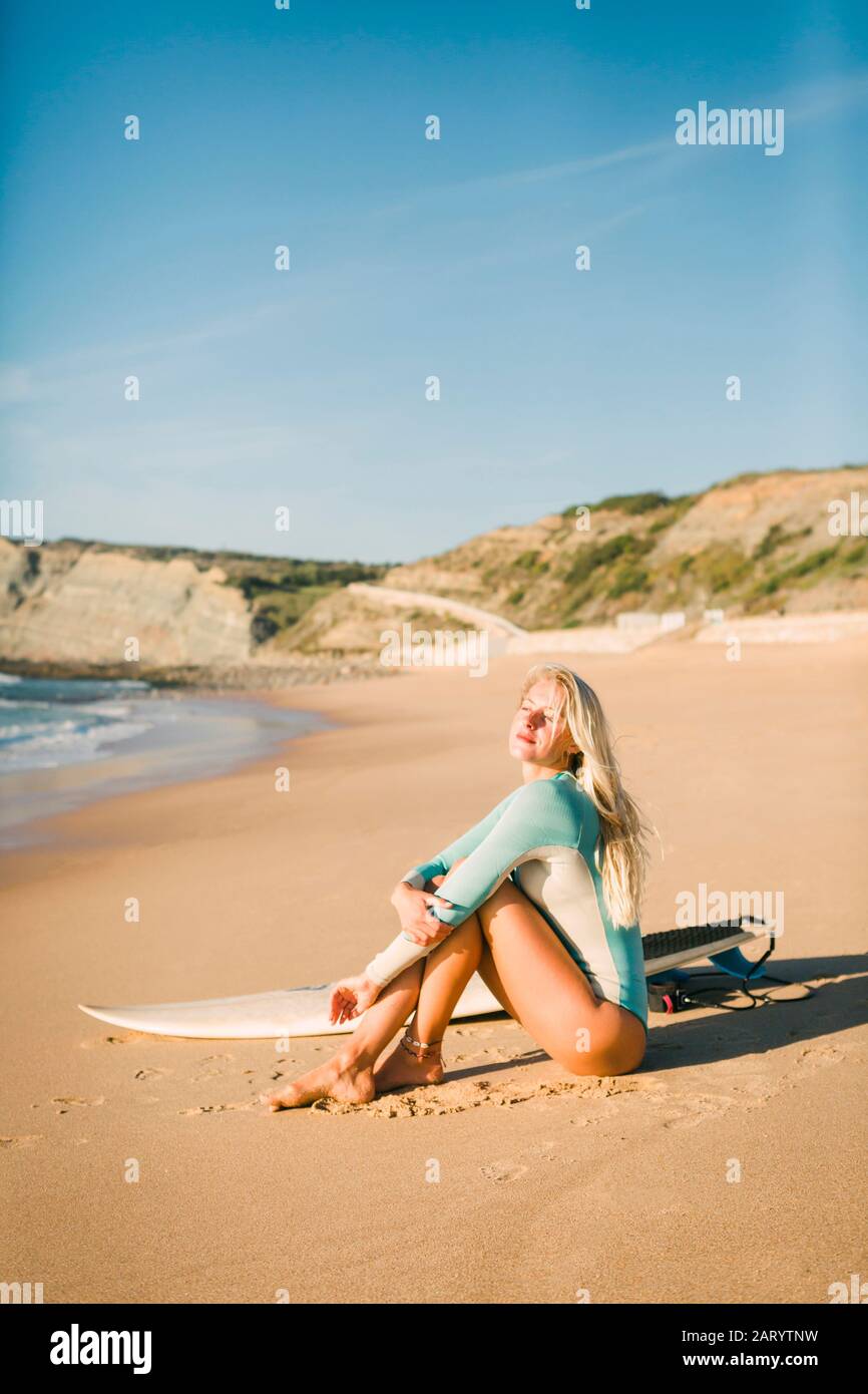 Femme assise à côté de la planche de surf sur la plage Banque D'Images