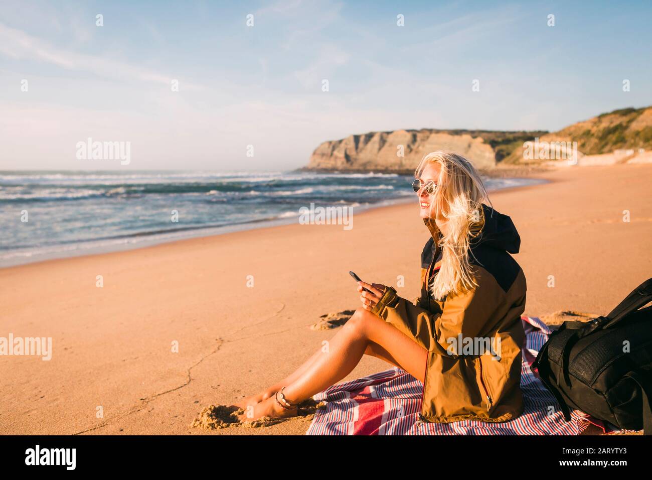 Femme tenant le téléphone assis sur la plage Banque D'Images