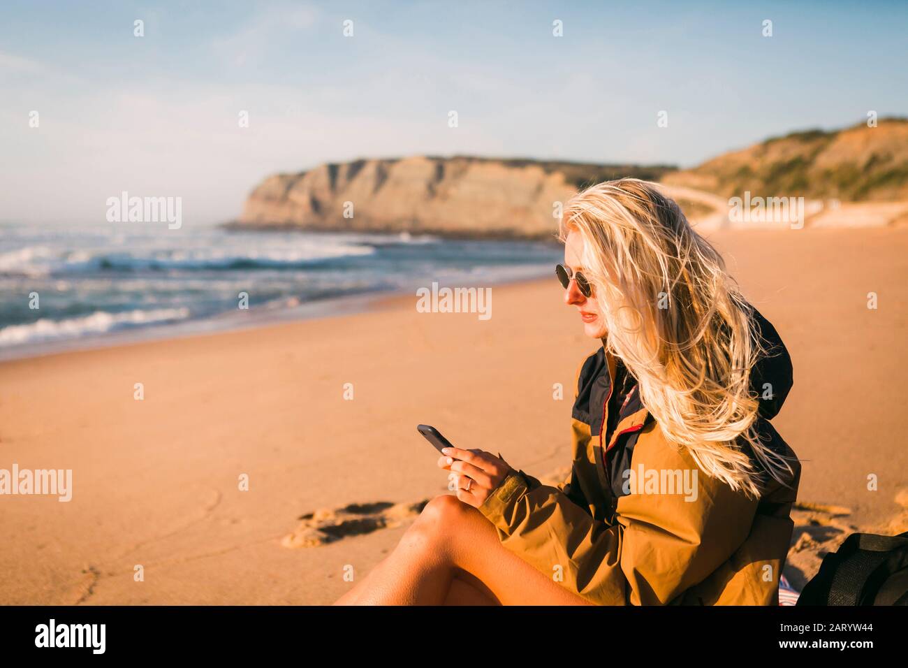 Femme tenant le téléphone assis sur la plage Banque D'Images