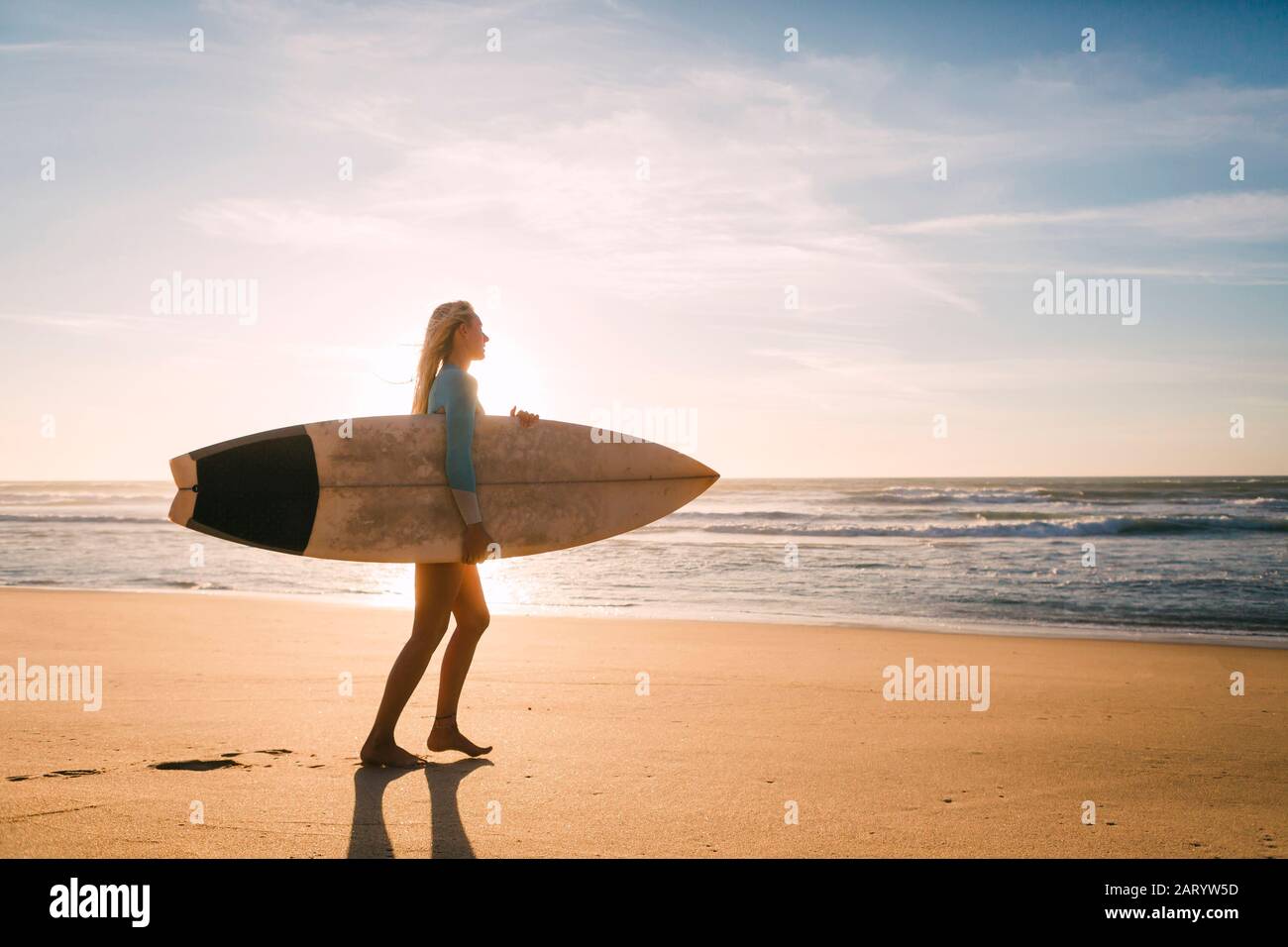 Femme portant une combinaison tenant une planche de surf sur la plage Banque D'Images
