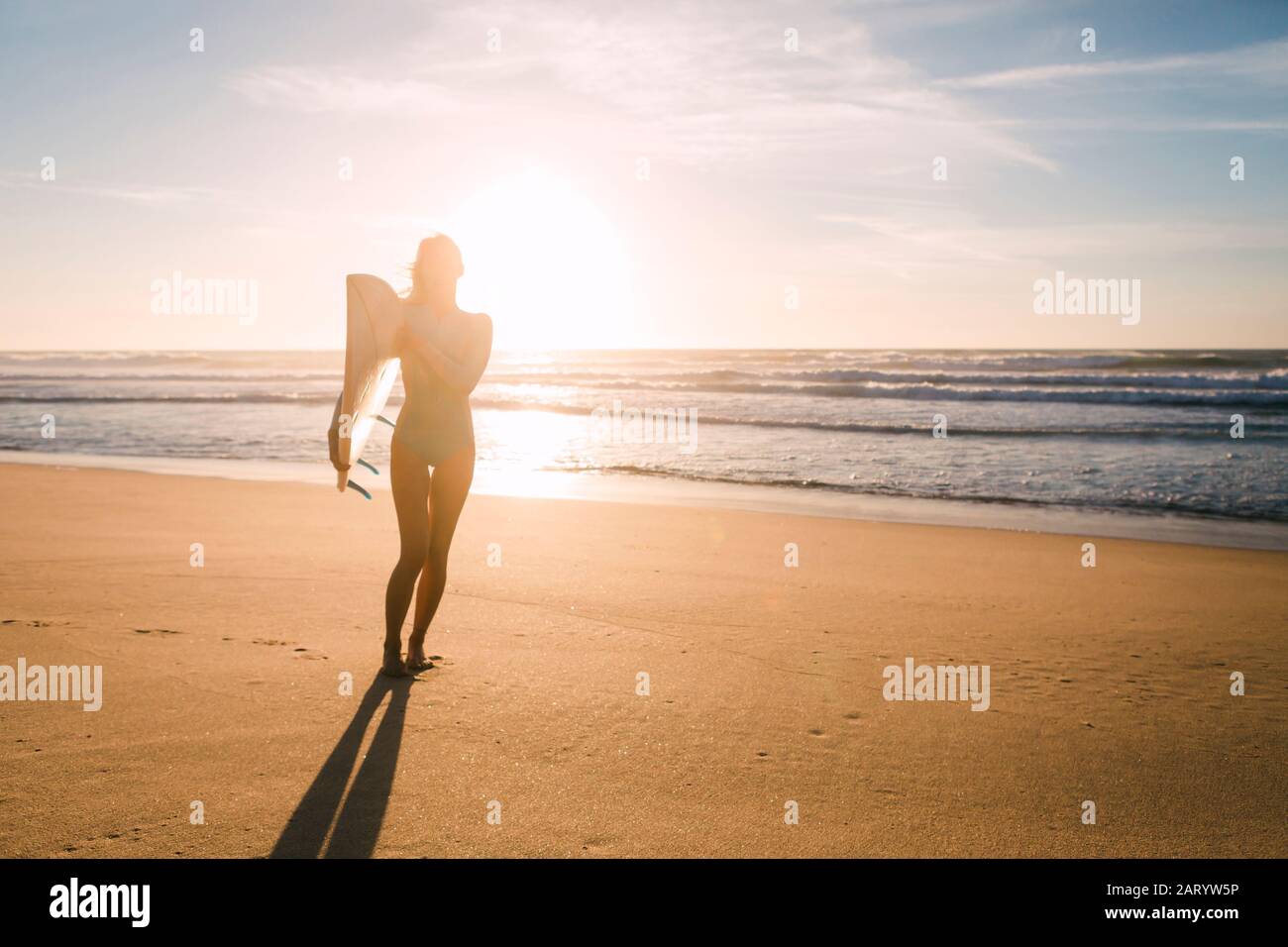 Femme tenant une planche de surf contre la lumière du soleil sur la plage Banque D'Images