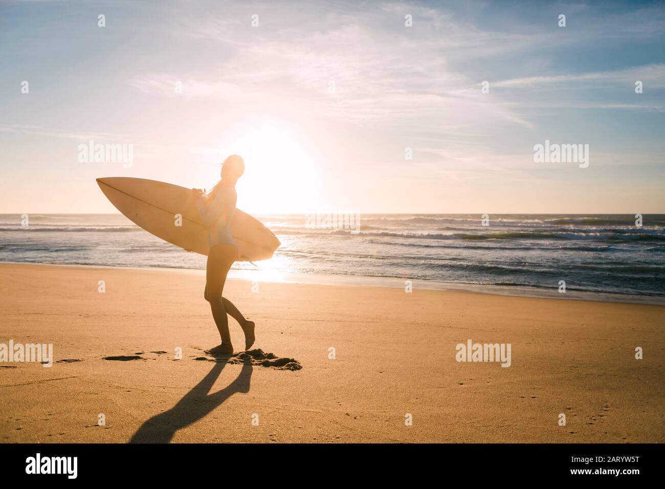 Femme tenant une planche de surf contre la lumière du soleil sur la plage Banque D'Images