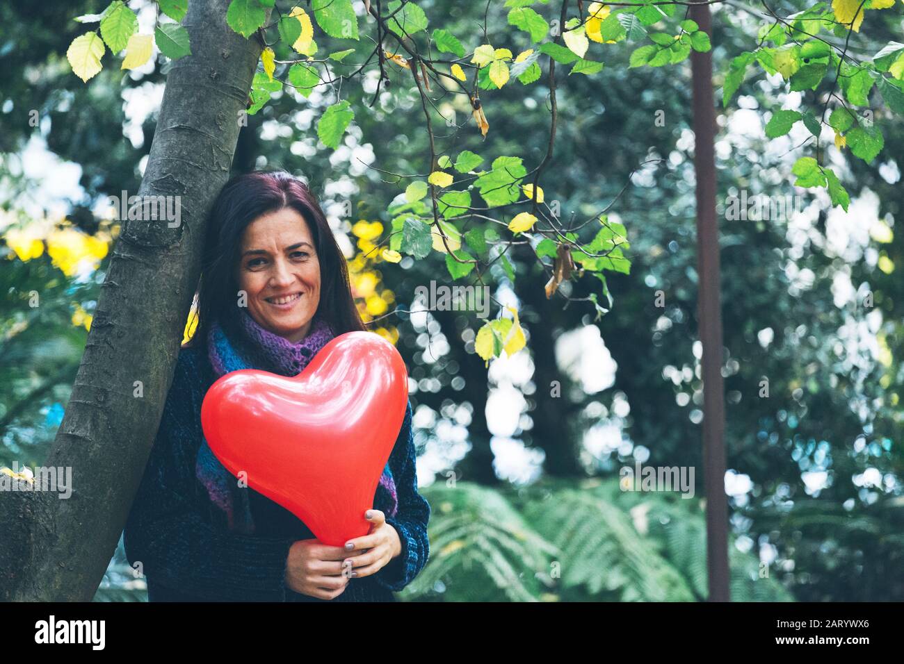 Femme souriante tenant le ballon de coeur près des arbres Banque D'Images