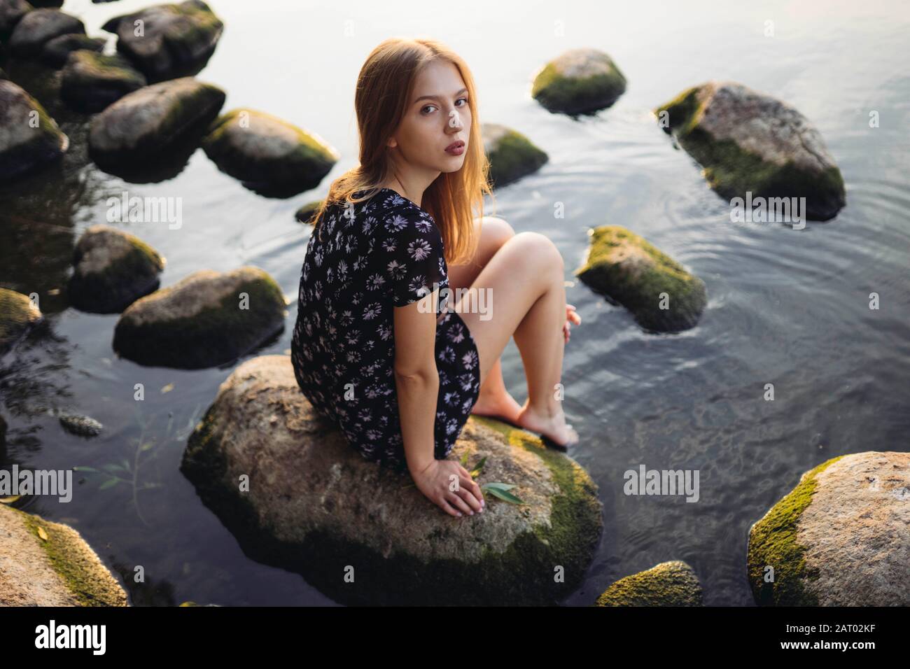 Femme portant une robe noire assise sur le rocher en mer Banque D'Images