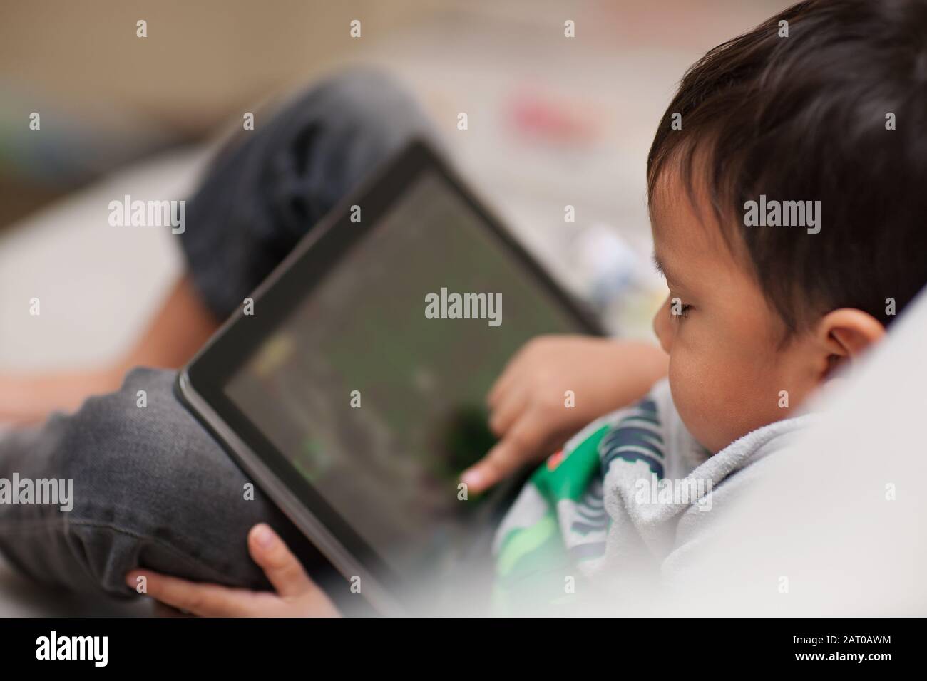 Un tout-petit non supervisé utilisant une tablette à la maison qui est détendu assis sur un canapé et à l'aide de son doigt sur l'écran tactile. Banque D'Images