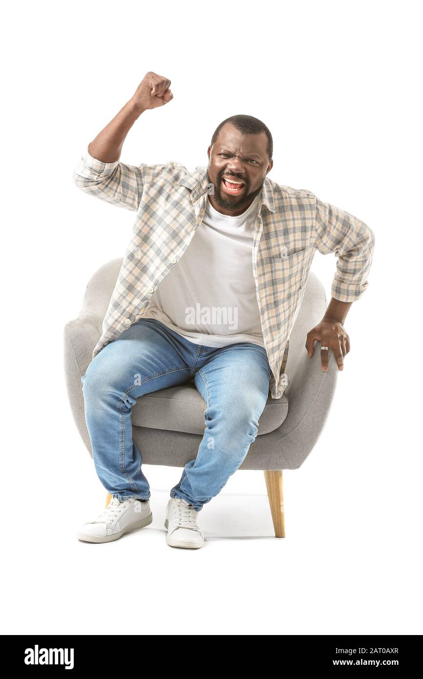 Homme affectif afro-américain regardant la télévision tout en étant assis dans un fauteuil sur fond blanc Banque D'Images