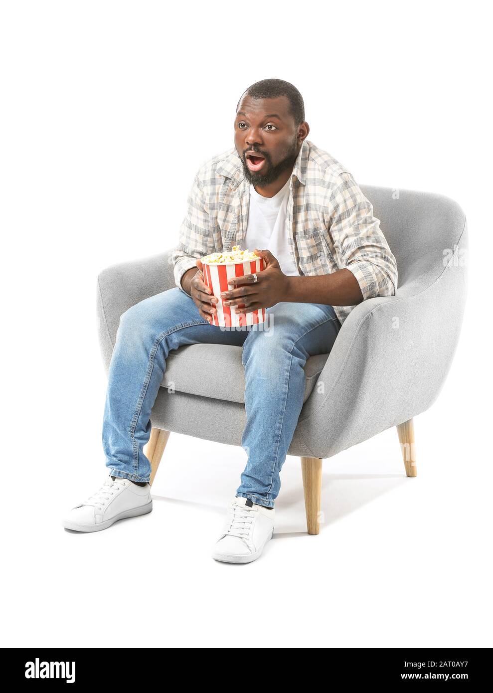 Homme affectif afro-américain avec pop-corn regardant la télévision tout en étant assis dans un fauteuil sur fond blanc Banque D'Images