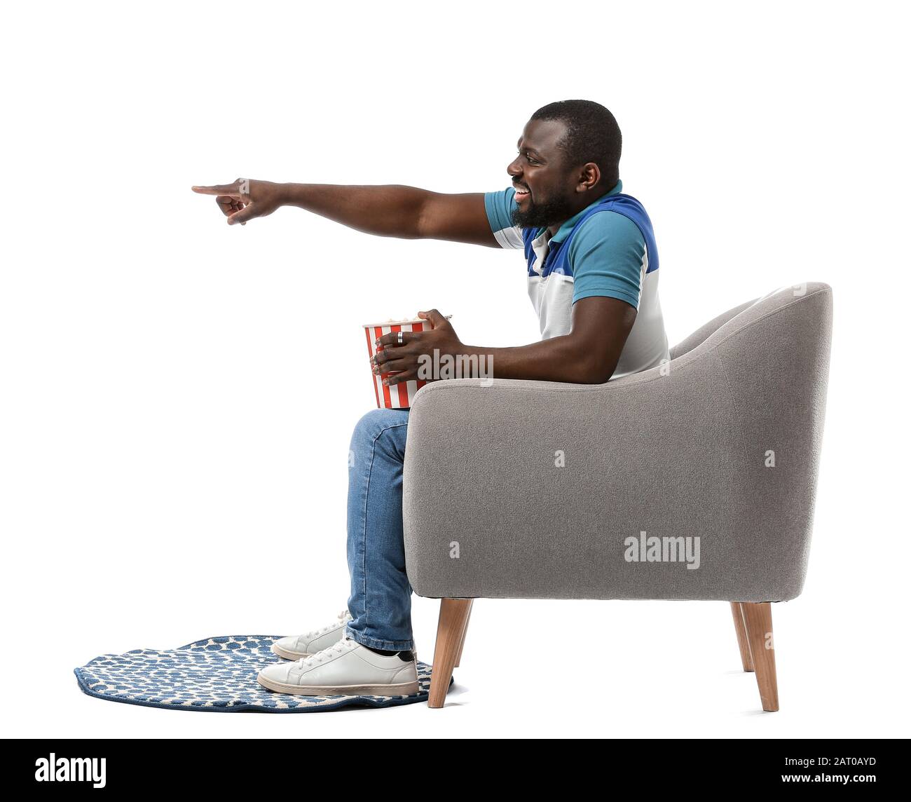 Homme afro-américain avec pop-corn regardant la télévision tout en étant assis dans un fauteuil sur fond blanc Banque D'Images