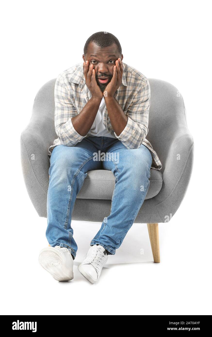 Homme affectif afro-américain regardant la télévision tout en étant assis dans un fauteuil sur fond blanc Banque D'Images