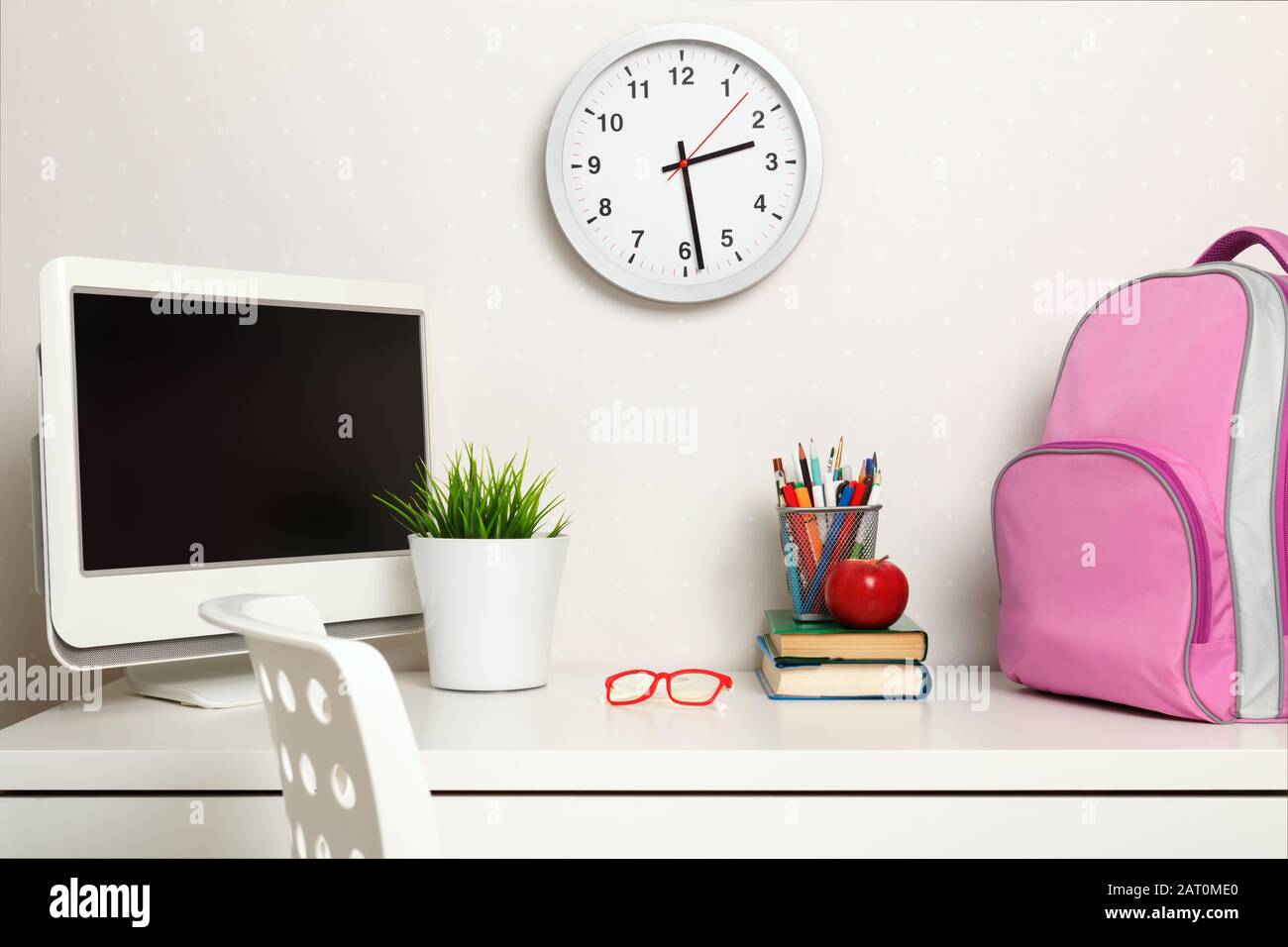 Une écolière sur le lieu de travail sur les murs de lumière de fond. Sur la table livres sac à dos ordinateur papeterie verres. Banque D'Images