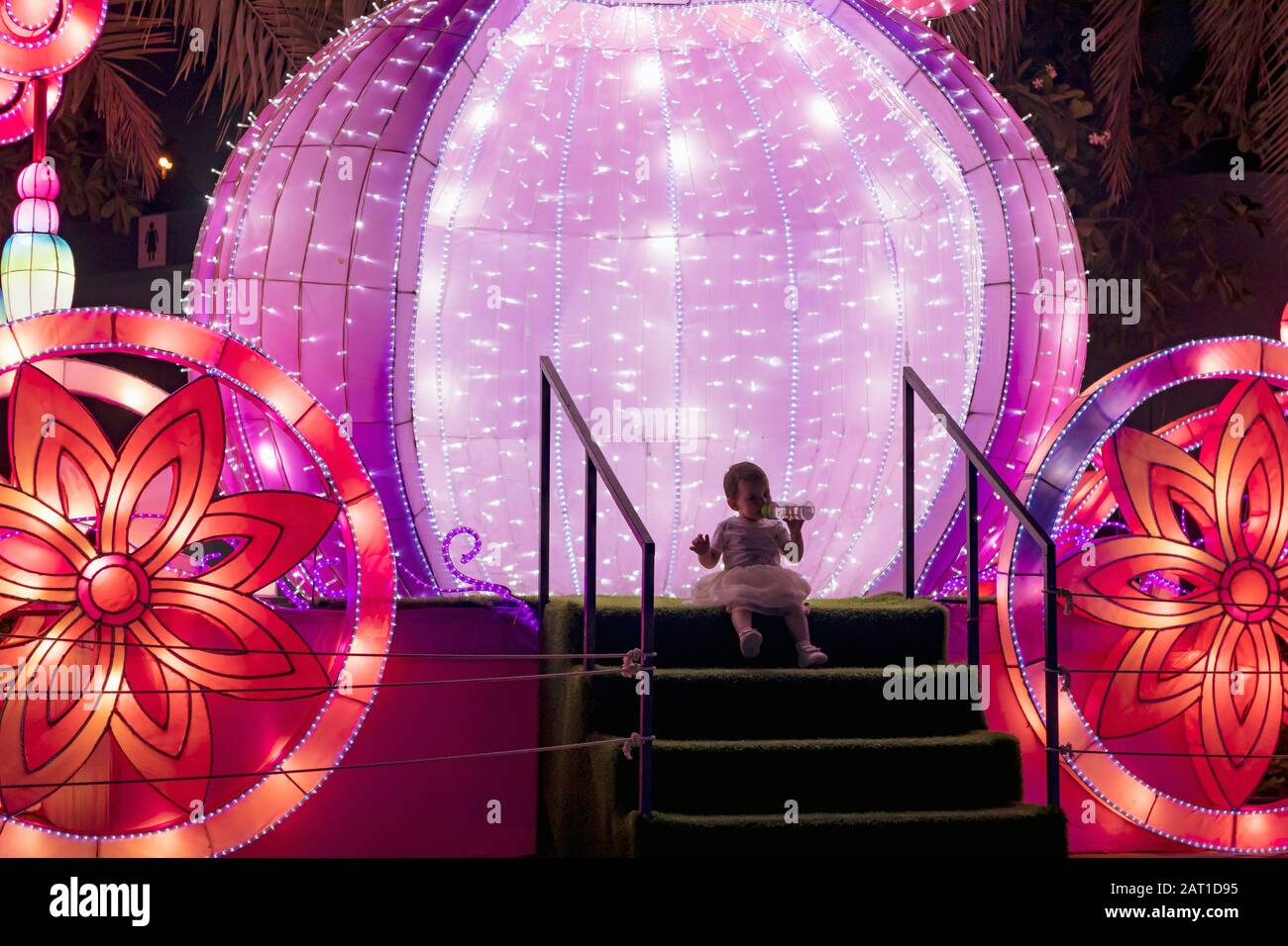 Une jolie petite fille buvant de l'eau de sa petite bouteille dans l'autocar de cendrillon dans le jardin brillant de Dubaï la nuit. Banque D'Images