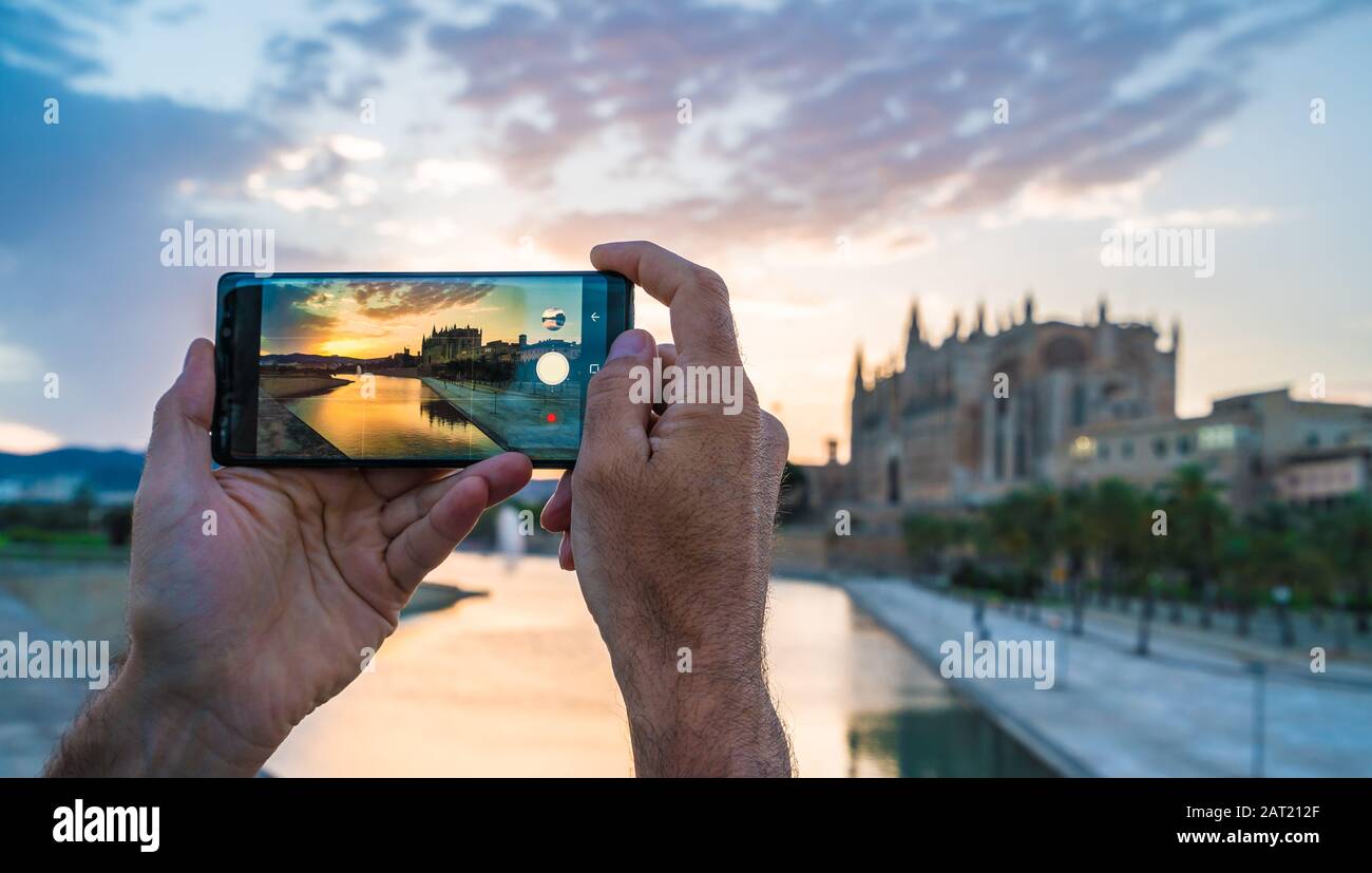 Les hommes utilisant son smartphone pour prendre une photo dans les îles de Palma de Majorque au coucher du soleil. En Arrière-Plan Cathédrale La Seu Banque D'Images