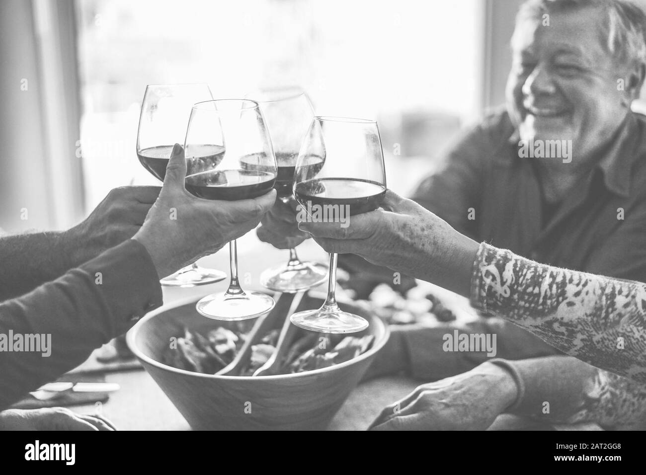 Joyeux amis seniors qui s'amusent à tricher avec du vin rouge - des personnes mûres qui mangent au dîner et rient ensemble - montage noir et blanc - Focus on bot Banque D'Images