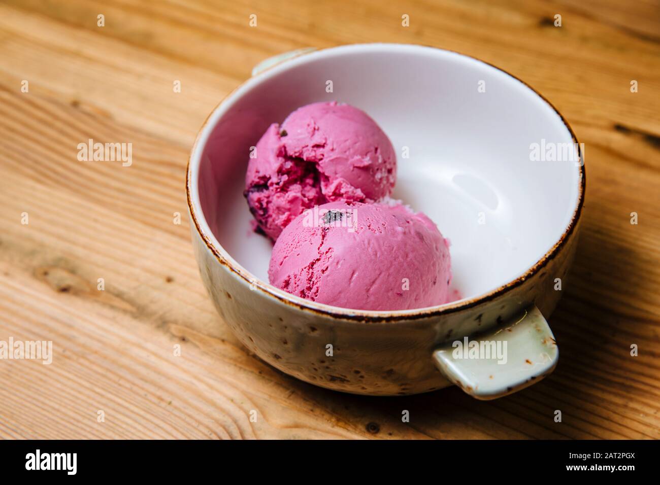 Deux boules de glace rose dans un bol sur une table en bois. Banque D'Images