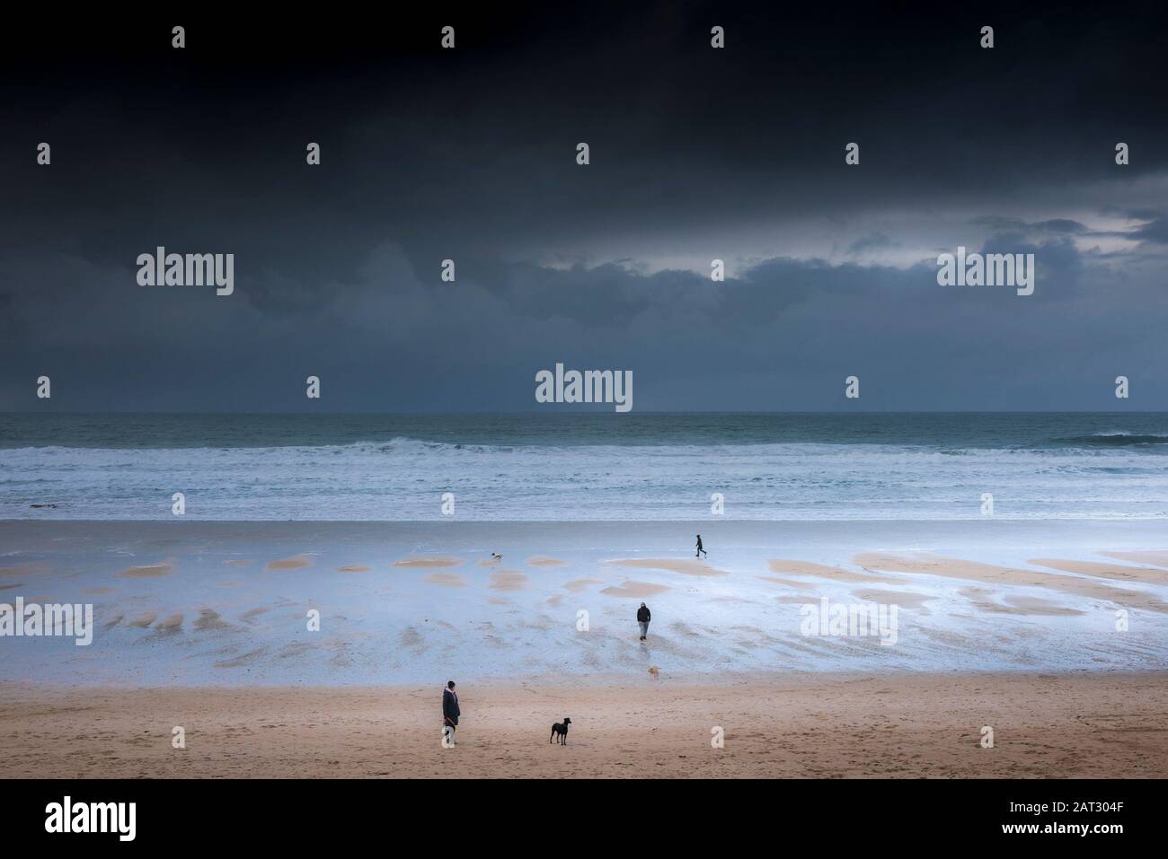 Les marcheurs de chiens et leurs animaux de compagnie sur la plage de Fistral alors que des nuages de pluie sombre approchent Newquay à Cornwall. Banque D'Images