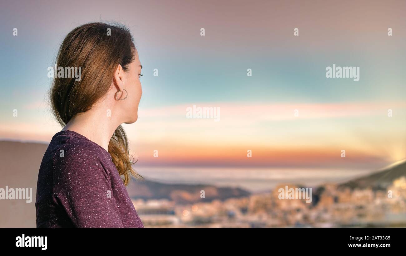 Portrait d'une femme rêvant, regardant la ville et la mer à l'heure d'or, vue sur le profil Banque D'Images