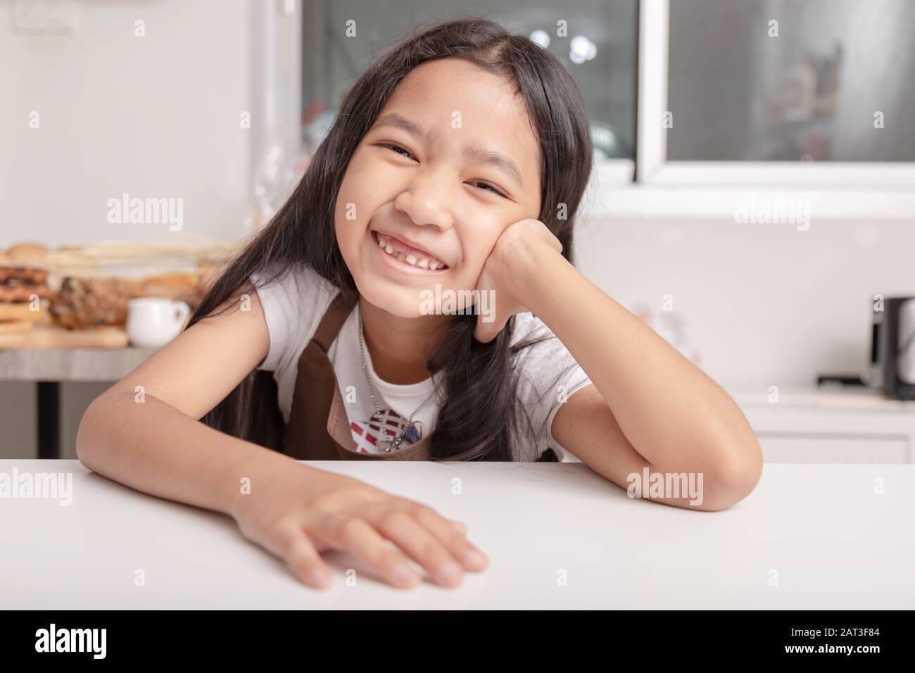 Une petite fille asiatique souriante a vu sa dent cassée sur une table de cuisson blanche dans la cuisine avec bonheur. Banque D'Images