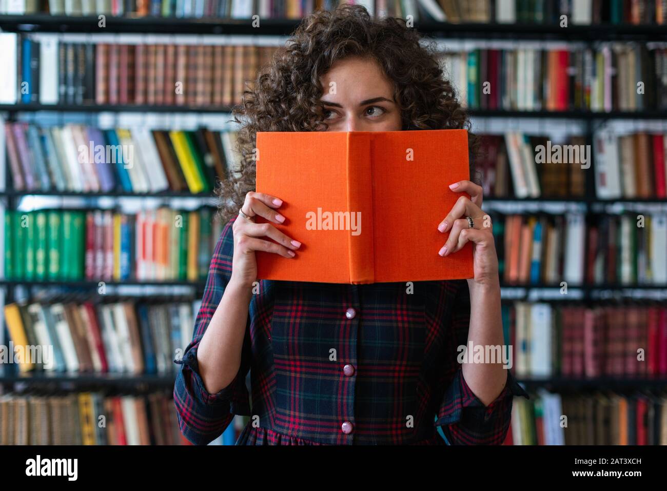 Une fille ludique tenant un livre couvrant son visage et regardant vers le côté. Livre Couverture Rigide Banque D'Images