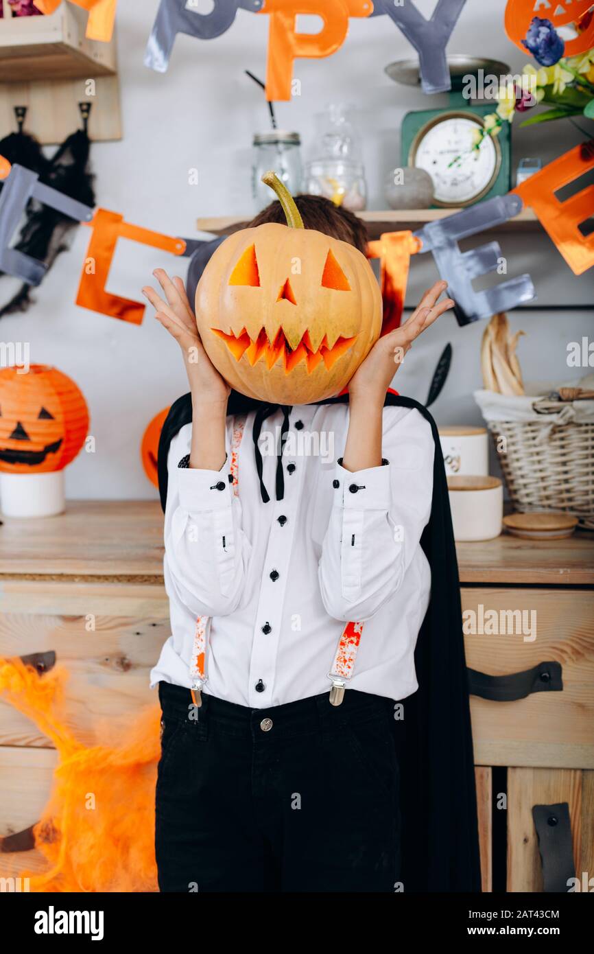 Garçon debout dans une robe mascarade tenant une citrouille et cacher son visage - image verticale Banque D'Images