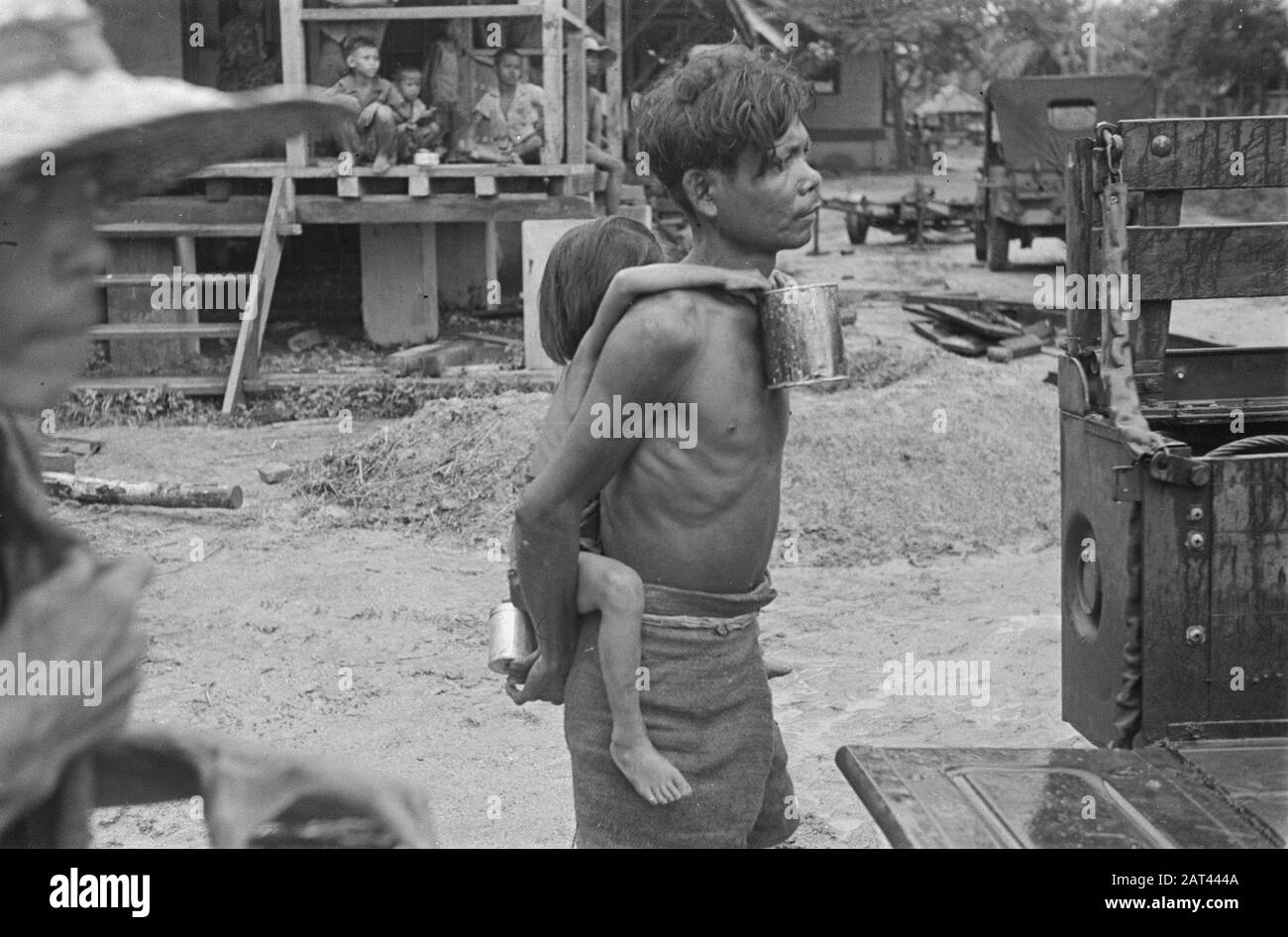 Photo Reportage Palembangs homme indonésien avec enfant au dos. L'enfant a un look. Les jeeps sont affichés. Date : Janvier 1947 Lieu : Indonésie, Antilles Néerlandaises De L'Est, Palembangs, Sumatra Banque D'Images