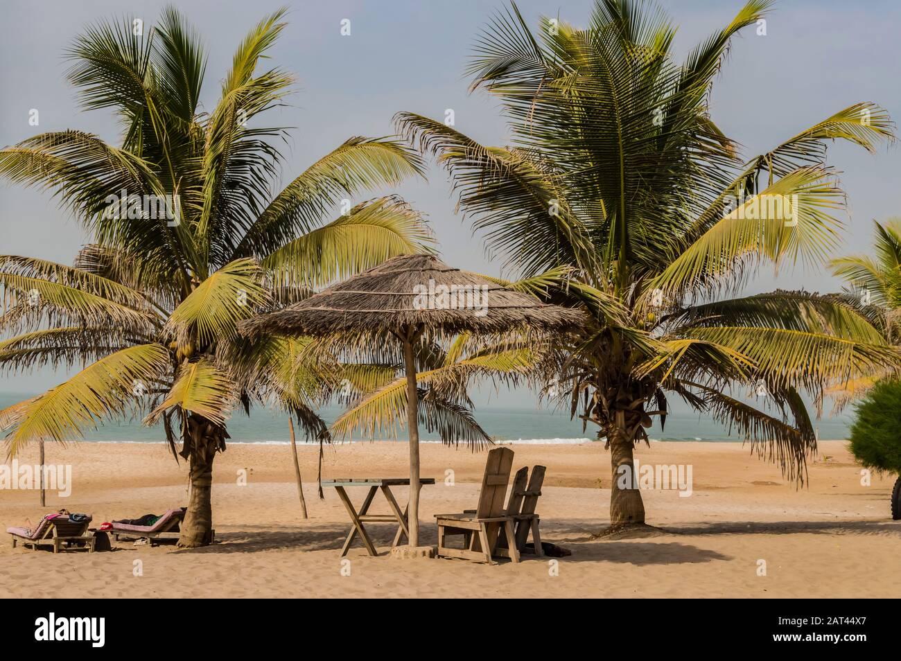 Deux chaises et une table basse sous une feuille de palmier et un parasol en bois sur la plage de Bijilo en Gambie Banque D'Images Deux chaises et une table basse sous une feuille de palmier et un parasol en bois sur la plage de Bijilo en Gambie Banque D'Images