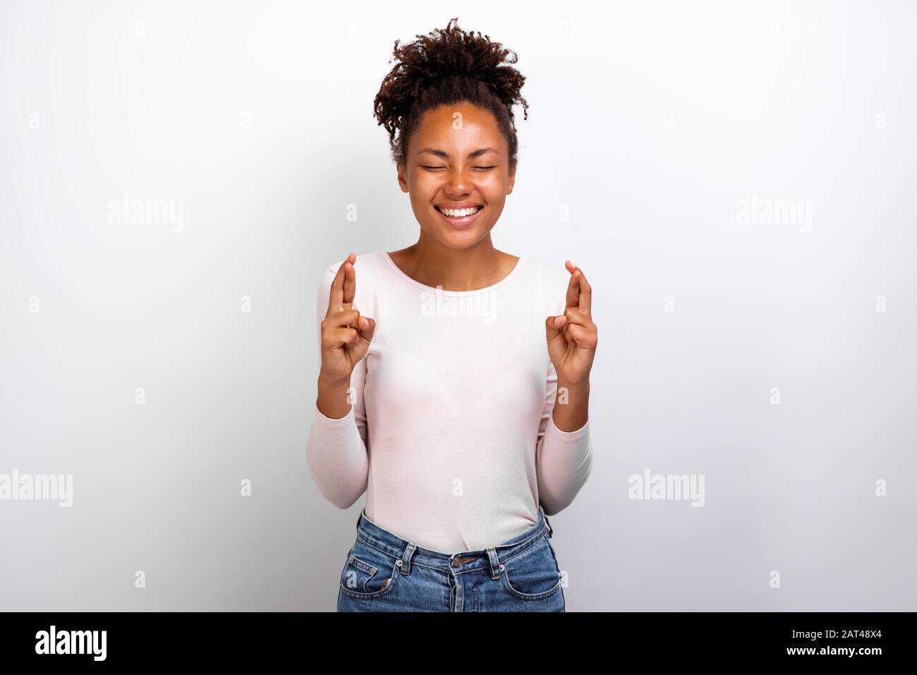 Mignonne femme mulatto croisant ses doigts et souhaitant bonne chance - image Banque D'Images
