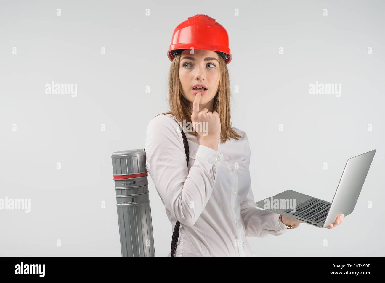 Femme architecte se tient avec un tube derrière son dos tenant l'ordinateur portable et regarder perdu dans la pensée Banque D'Images